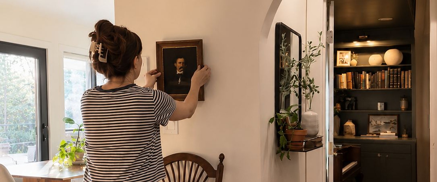 Shelby hanging a small antique portrait beside a plaster archway