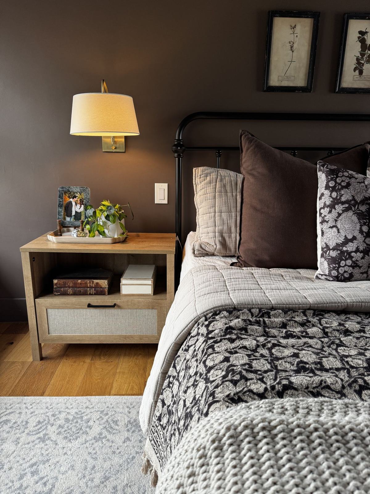 Bedroom with deep brown walls, an iron bed and a brass sconce