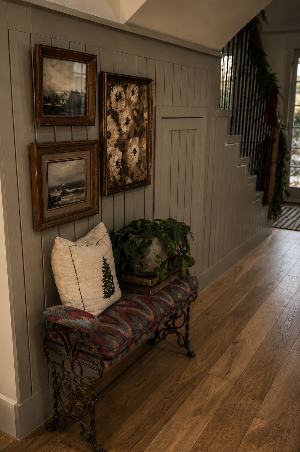 Entry bench with kilim upholstery, gold framed paintings and garland on the stair rail