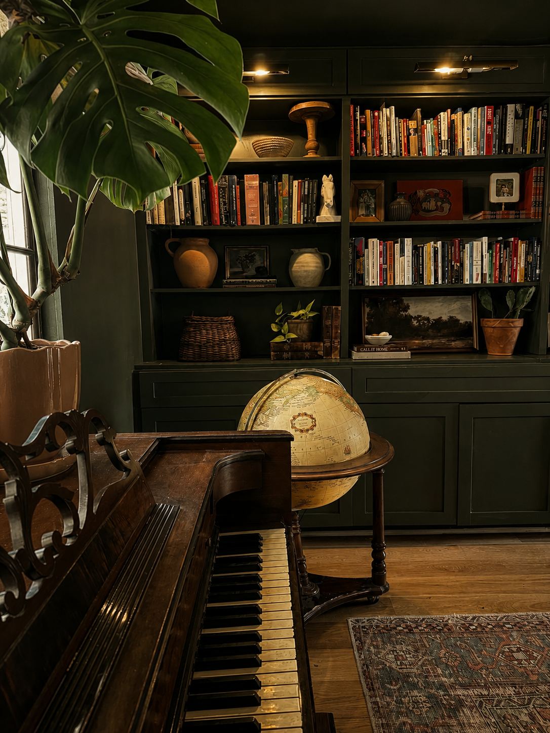 Study with deep green built-in shelves, an upright piano and a globe